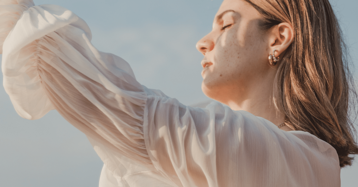 This is a picture of a woman in a light white blouse holding her hand up to sheild her face from the sun. It links to a blog post about sun protection and summer skin care tips.